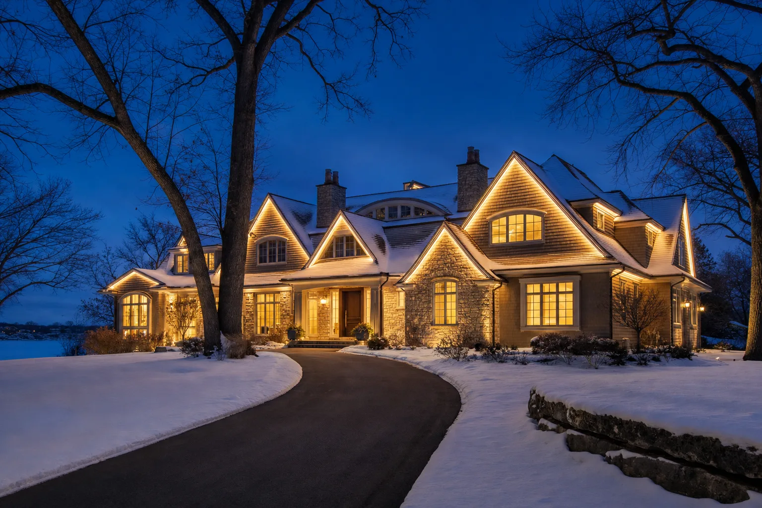 Wayzata-style Twin Cities lakefront home with permanent LED channel lighting on rooflines and dormers at blue hour